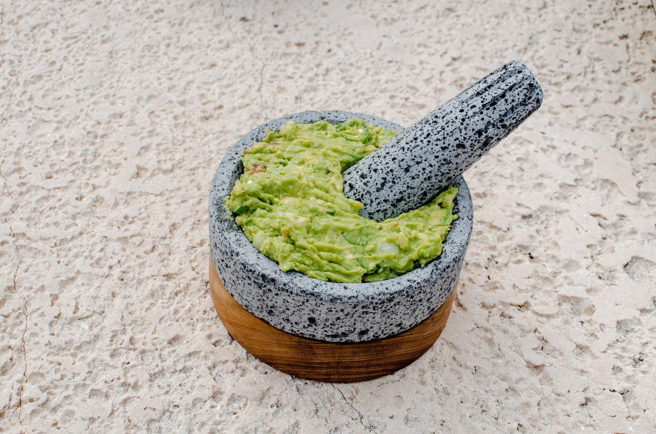 Authentic Mexican molcajete made of volcanic rock, perfect for grinding herbs and spices. Rough-textured surface and deep bowl shape. Pictured on wooden surface with traditional ingredients like chili peppers, garlic, and tomatoes